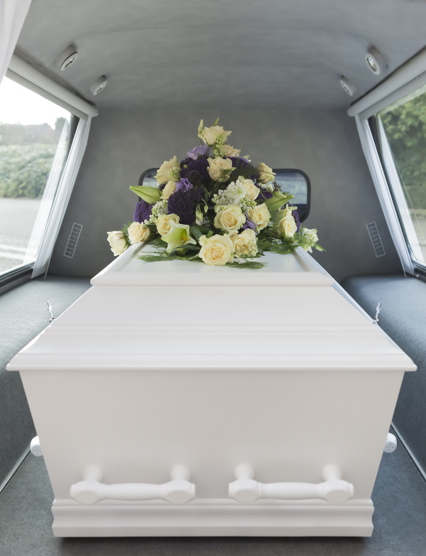 A picture of a coffin inside a hurst, with flowers on top